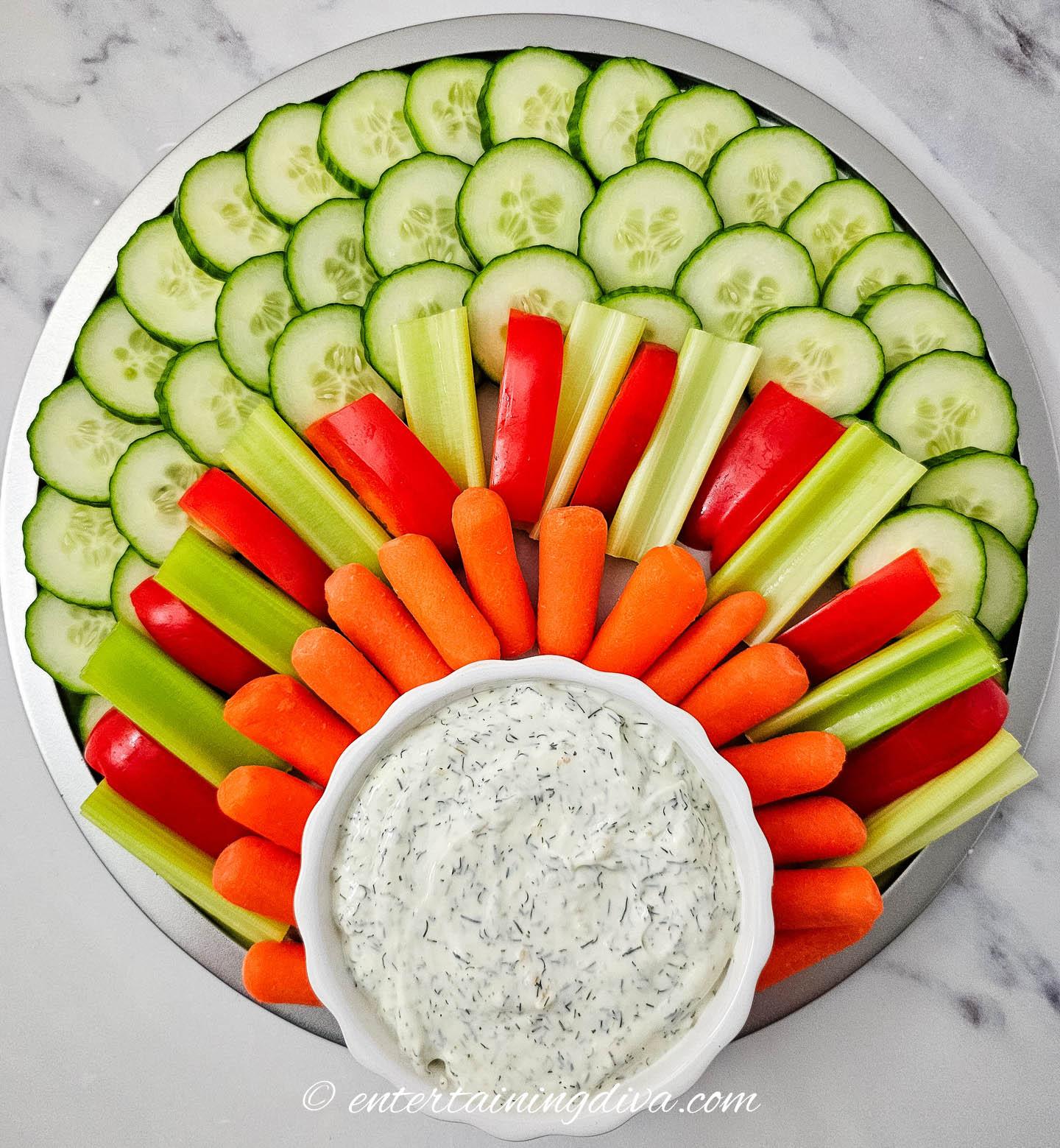 cucumbers, celery, red peppers and carrots on a circular tray with a bowl of veggie dip